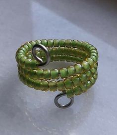 a green beaded bracelet sitting on top of a white table next to a metal hook