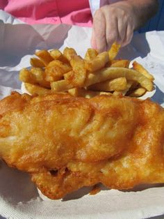 fish and fries are sitting on a paper wrapper with someone reaching for the food