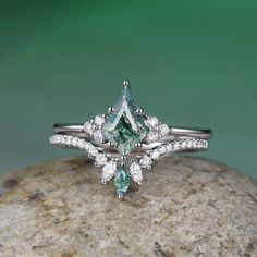 a green and white diamond ring sitting on top of a rock with diamonds around it