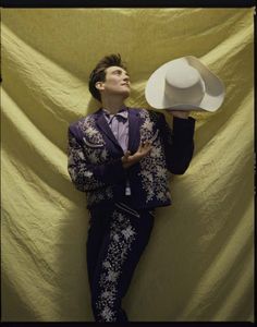 a man in a suit and hat leaning against a wall