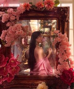 a woman sitting in front of a mirror surrounded by flowers