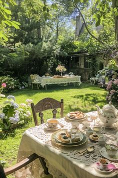 a table with plates and cups on it in the middle of a lawn area surrounded by flowers