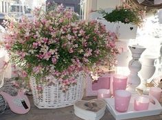 pink flowers in a white basket on a table with candles and other items around it