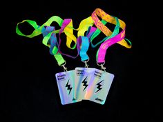 three lanyards with neon colored ribbons and tags attached to them on a black background