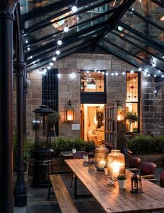 a wooden table sitting under a glass roof next to a light filled building with windows