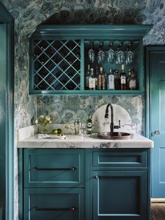 a kitchen with green cabinetry and marble counter tops, wine bottles on the shelves