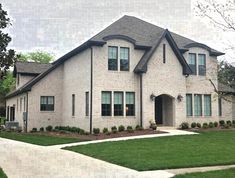 a white brick house with green grass and trees in the front yard on a cloudy day