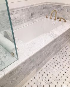 a bathroom with marble tile and gold faucet, shower head, and bathtub