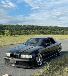 a black car parked in a parking lot next to some grass and trees on a sunny day