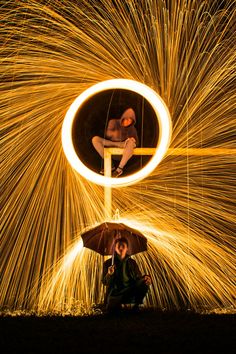 a person sitting on the ground with an umbrella in front of some spinning steel wool