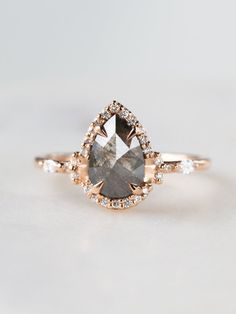 an engagement ring with a pear shaped gray diamond surrounded by small white and brown diamonds