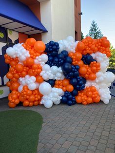 an orange, white and blue balloon arch on the side of a building with trees in the background