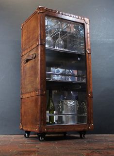 a wooden case with glass bottles and wine glasses on it's sides, sitting on top of a brick floor