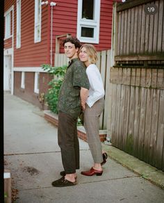 two people standing next to each other in front of a red house with a white door