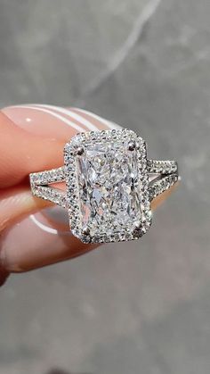 someone is holding an engagement ring with a cushion cut diamond in the center and two rows of diamonds on each side