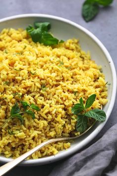 a white bowl filled with yellow rice and garnished with green leaves on top