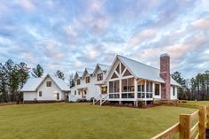 a large white house sitting on top of a lush green field next to a wooden fence