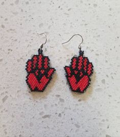 red and black beaded earrings with hand prints on them sitting on a white surface