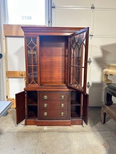 an old wooden cabinet with glass doors and drawers in a garage area next to a bench