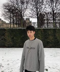 a young man standing in the snow wearing a gray sweatshirt