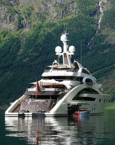 a large white boat floating on top of a lake next to a lush green hillside