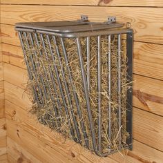 a metal cage with hay in it hanging on the side of a wooden wall