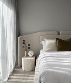 a white bed sitting next to a window with sheer curtains on the windowsills