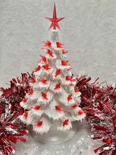 a white christmas tree with red and silver tinsel around it on a table top