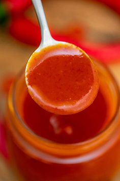 a spoon full of ketchup sitting on top of a jar filled with sauce