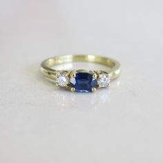 Sapphires and diamonds are the perfect pairings. This sapphire is set east to west and adorned with two bright white round brilliant diamonds set in 18k yellow gold. Metal: 18K Yellow Gold Sapphire: 6 x 4.5 MM Diamonds: .20 CTW VS1-2 G Size: 6 For a greater selection of jewelry please visit our website at www.BlackMarketLLC.com If you have any questions about this product or if we can help you with any of our other products please contact us through Etsy or our website at www.blackmarketllc.com. Sapphire And Diamond Three Stone Ring, Timeless Yellow Gold Sapphire Ring With Center Stone, Elegant Gold Ring With Lab-created Sapphire, Elegant Yellow Gold Lab-created Sapphire Ring, Timeless Sapphire-colored Cubic Zirconia Ring, Timeless Cubic Zirconia Ring In Sapphire Color, Yellow Gold Sapphire Ring With Brilliant Cut Cubic Zirconia, Timeless Gold Sapphire Ring With Single Cut Diamonds, Yellow Gold Three-stone Sapphire Ring