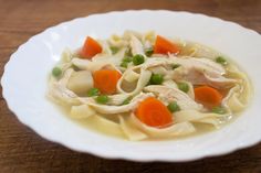 a bowl of chicken noodle soup with carrots and peas