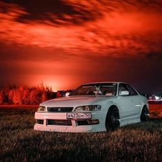 a white car parked on top of a lush green field under a red sky at night