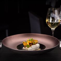 a glass of white wine and a plate with food in it on a black table