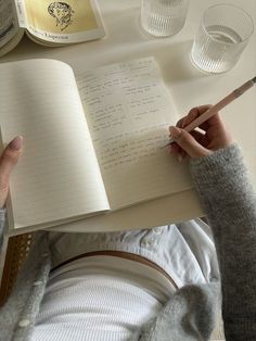 a person sitting at a table with an open notebook and pen in their hand, next to empty glasses