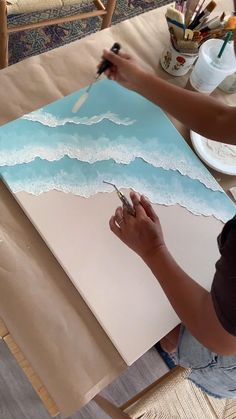 a woman is painting an ocean scene with acrylic paint on paper and scissors