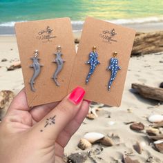 two small earrings with blue and white polka dots are held up in front of the ocean