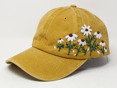 a yellow hat with daisies embroidered on the front and back side, sitting on a white surface