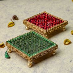 two pieces of jewelry sitting on top of a table next to gold and green decorations