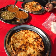 two pizzas on pans sitting on top of a red table