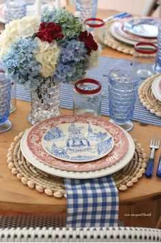 a table set with blue and white plates, napkins and flowers in a vase