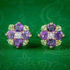 A colourful pair of Suffragette tribute earrings decorated with a cluster of four violet amethysts, four green peridots and a central brilliant cut diamond. This combination of gemstone colours often paid tribute to the women's Suffrage movement which took place in the early 20th Century and symbolised; Violet for Loyalty, White for Purity and Green for Hope, or Give Women Votes! The stones are all set in a 9ct gold gallery and fitted with butterfly stud backs complete with Birmingham hallmarks. Purple Multi-stone Earrings For Anniversary, Suffragette Jewellery, Gemstone Colours, Suffrage Movement, Gold Gallery, Edwardian Style, Silver Lockets, Edwardian Fashion, Green Peridot