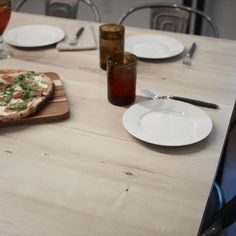 a pizza sitting on top of a wooden cutting board next to plates and glasses filled with drinks