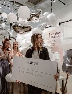 a group of women standing next to each other in front of balloons and holding a large check