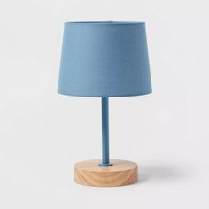 a blue lamp on a wooden base with a light blue lampshade behind it