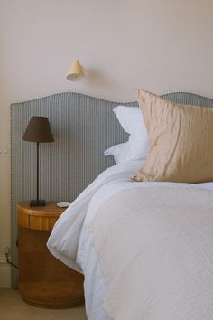 a bed with white sheets and pillows next to a lamp on a nightstand in a bedroom