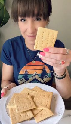 a woman holding up a cracker on top of a white plate next to a pile of crackers