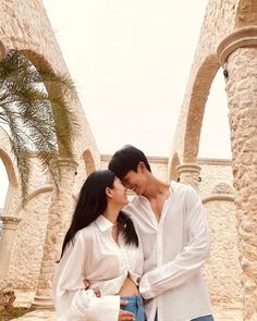 a man and woman standing next to each other in front of stone archways with palm trees