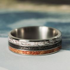 a wedding ring with two different colored bands on it's side, sitting on top of a blue and white table cloth