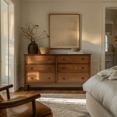 a bedroom with a bed, dresser and chair next to a large painting on the wall