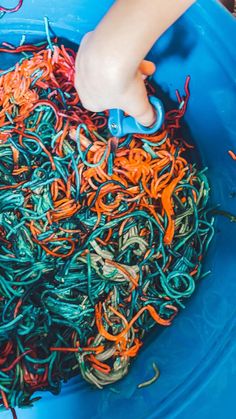 a child's hand is in a blue bucket filled with colored shredded paper and scissors